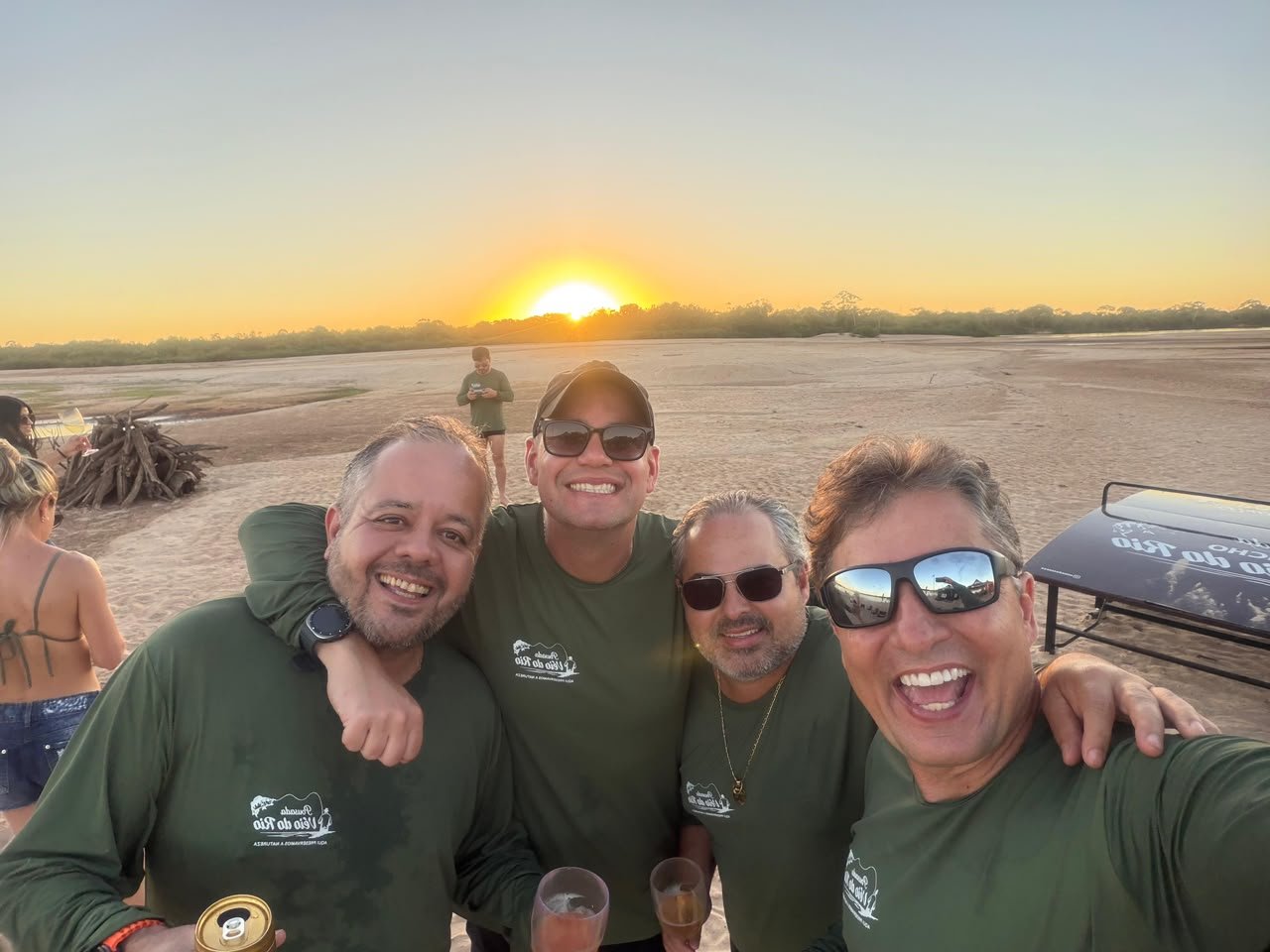 Amigos com camisas da pousada no pôr do sol da praia